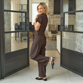 Side view of woman in a polka dot jumpsuit standing in a modern living room with open doors.