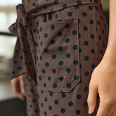Close up details of brown polka dot women's jumpsuit with pockets and a tie belt, visible Albion logo and blurred background