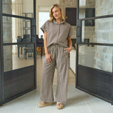 Woman in a chic matching set outfit—button down shirt and striped pants, standing in a modern interior.