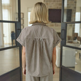 Back view of woman wearing a short-sleeved button up shirt in brown and cream stripes.