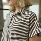 Close-up of a woman wearing a brown and cream striped shirt with a blurred background
