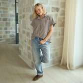Woman wearing a short-sleeve button down shirt and jeans standing against a stone wall.