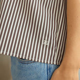 Close-up of a person wearing a brown and cream striped shirt with Albion logo, paired with blue jeans.