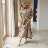 Woman wearing a gingham maxi dress standing in a well-lit room with large windows.