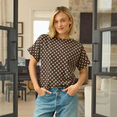 Woman wearing a brown polka dot shirt and blue jeans standing in a modern living room.