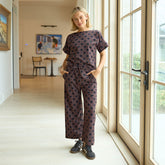 Woman in a polka dot brown matching set outfit standing by a large window in a home.