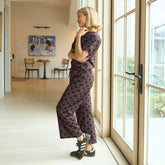 Woman in a polka dot, brown women's matching set standing by a large window in a home.