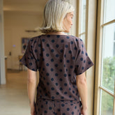 Woman wearing a brown polka dot outfit standing by a window.