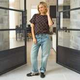 Woman standing in a modern interior space wearing a polka dot shirt and jeans.