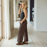 Woman standing in a modern home interior wearing a black top and polka dot brown women's pants.