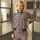 Woman wearing a brown, floral bomber jacket with matching pants standing in a modern interior setting
