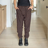 Woman wearing brown polka dot jogger pants with gold zippers and pocket details standing in a hallway.
