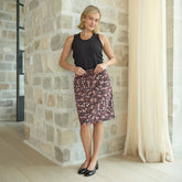 Woman wearing a black sleeveless top and flattering skirt standing against a stone wall.