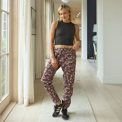 Woman wearing a black crop top and floral pants standing in a well-lit room.