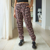 Woman wearing brown floral women's joggers with black sneakers in a hallway.