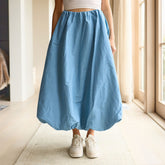 woman wearing a cute, blue bubble skirt and white sneakers in a bright hallway.