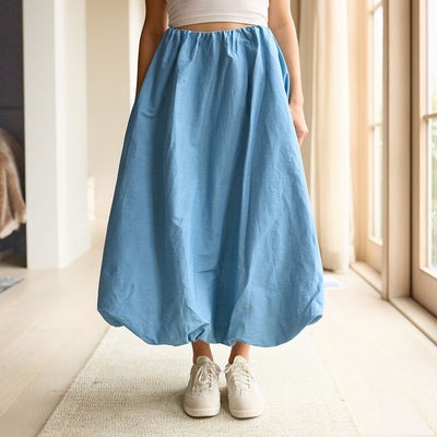 woman wearing a cute, blue bubble skirt and white sneakers in a bright hallway.