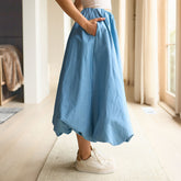 Side view of woman wearing a chambray bubble skirt with white sneakers in a room with light-colored walls and flooring.