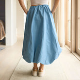 Back view of woman wearing a bubble skirt in light blue with sneakers, standing well-lit hallway.