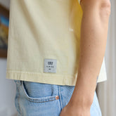 Close up of person wearing a light yellow shirt with a visible Albion brand label and denim skirt.