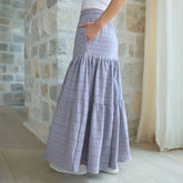 Woman wearing a maxi skirt with pockets in blue with a stone wall and curtain in the background