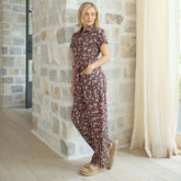 Woman in a flattering jumpsuit in brown floral print standing against a stone wall