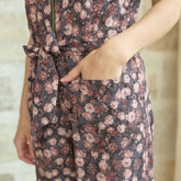 Close up of woman wearing a brown floral jumpsuit with her hand in her pocket and a visible Albion logo with a blurred background