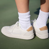 Rear view of Sea Salt and Honest Beige Sorel Ona Drift sneakers with tan heel accents and white ribbed socks