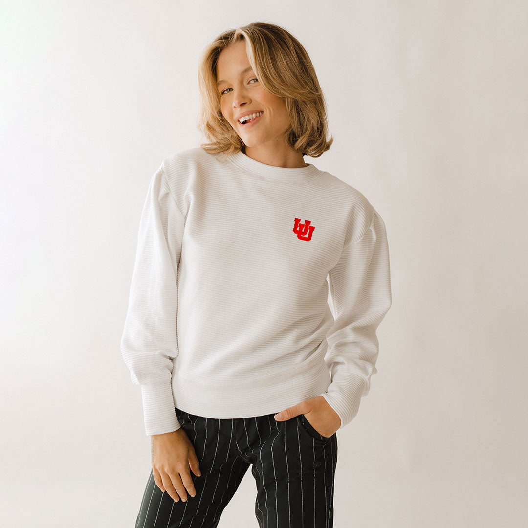 A woman smiling and wearing a white ribbed sweater with the University of Utah logo on the chest.