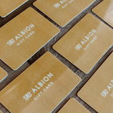 A collection of beige gift cards with the brand name 'ALBION' printed on them, arranged in a grid pattern on a wooden surface.