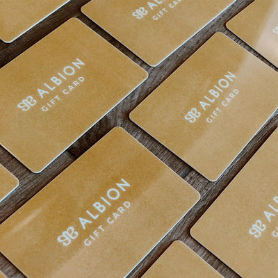 A collection of beige gift cards with the brand name 'ALBION' printed on them, arranged in a grid pattern on a wooden surface.