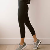 Side view of black Intention Flow Capris showcasing high-waisted capri fit on a model in a neutral room