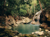 People swim in a turquoise pool beneath a waterfall in a lush Guatemalan forest