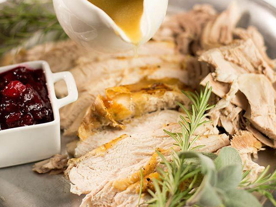 Close-up of sliced roasted turkey showcasing golden-brown skin with cranberry sauce, gravy, and fresh herbs