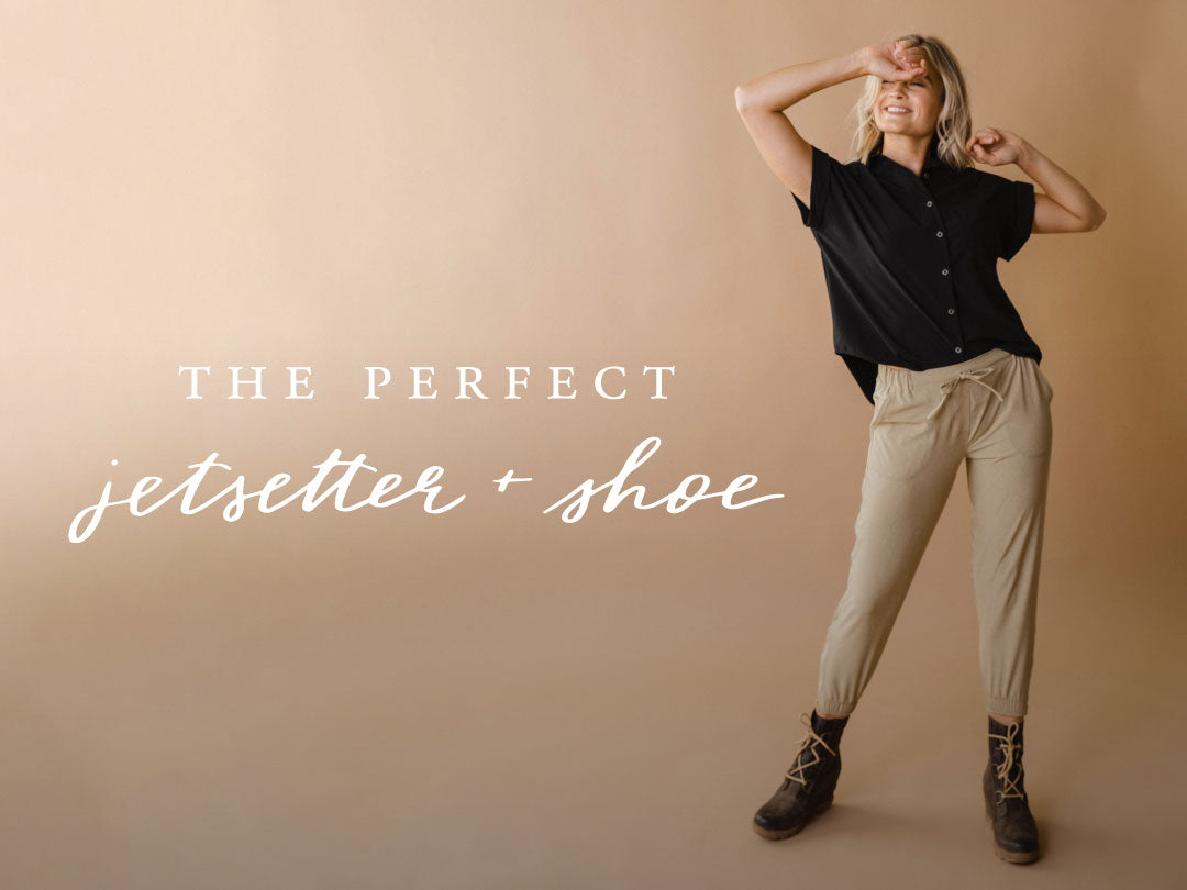 Model posing in a black top, beige Jetsetter pants, and black lace-up boots against a warm tan studio background