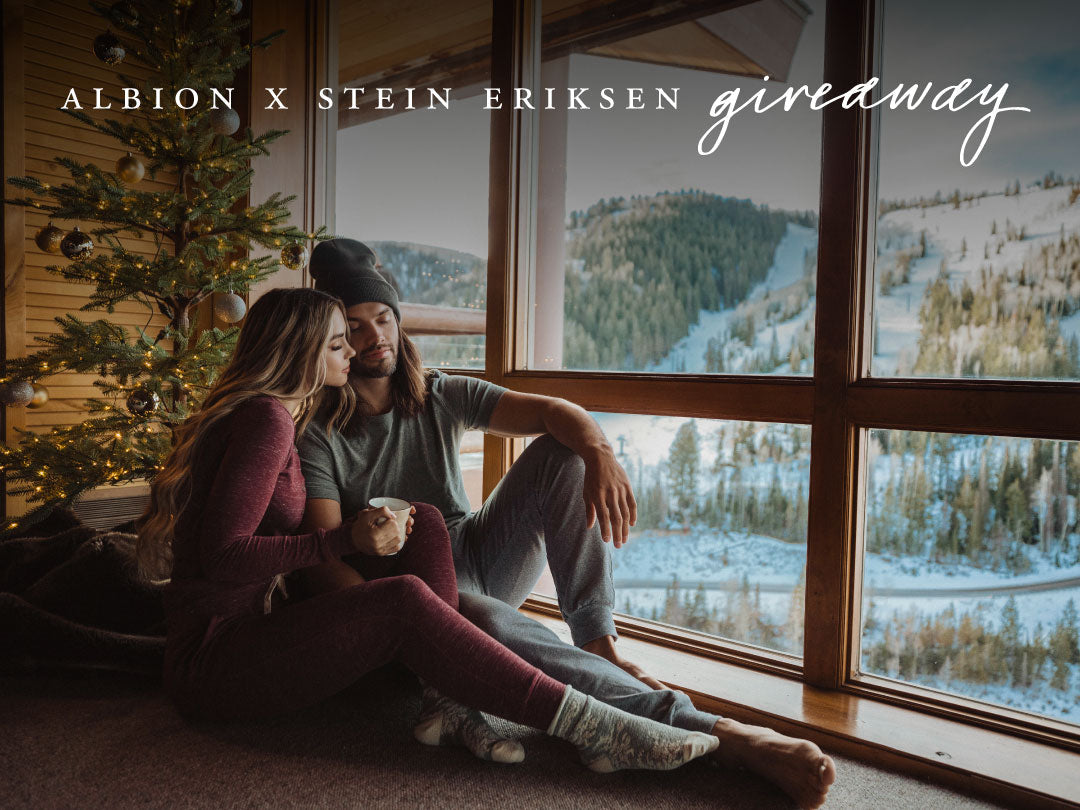Couple relaxing by a window overlooking snowy mountains for the ALBION X STEIN ERIKSEN giveaway