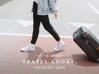 Traveler in black pants pulling a black suitcase along a street with text reading Five travel looks, one perfect pant