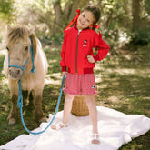 Young girl standing with a pony while wearing a cute, kids Disneyland outfit—kid's Mickey Mouse jacket in red with red gingham kid's Minnie Mouse shorts. 