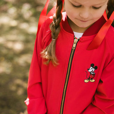 Close up of child wearing a kids Mickey Mouse jacket with embroidered Mickey and gold zipper details on a blurred background.