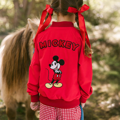 Child standing with a pony wearing a kid's Disney jacket—a red Mickey Mouse bomber jacket with kid's Disney shorts. 
