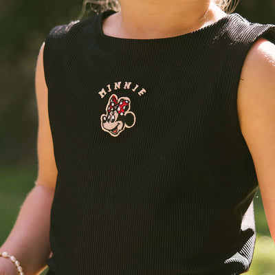Close up of a black Minnie Mouse Disney tank top for kids with embroidered Minnie details on a blurred natural background