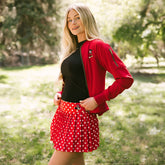 Woman standing in a park wearing the perfect Disney outfit—women's Disneyland jacket, women's Minnie tank top, and women's Disney tennis skirt in red polka dots. 