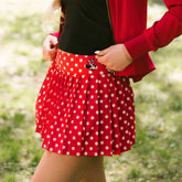 Close up of woman wearing red polka dot Disney tennis skirt on a blurred greenery background.