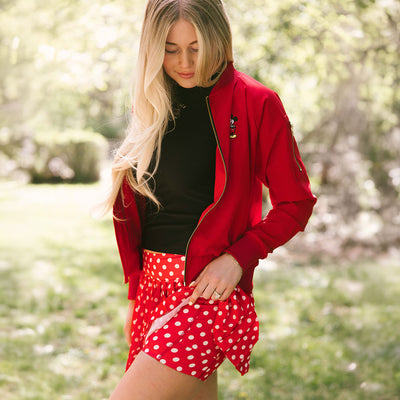 Woman standing in a garden wearing a Disney tennis skirt in red polka dot print with Minnie Mouse tank and red bomber jacket. 