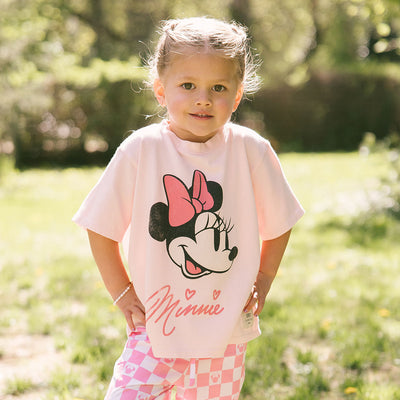 Young girl wearing the perfect Disney t-shirt for kids—pink Minnie Mouse tee with pink Disney pants for kids—on a blurred greenery background.