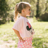 Young girl wearing a pink Minnie Mouse t-shirt for kids standing in a garden.