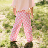 Back view of young girl wearing pink check kids pants for Disneyland on a blurred grassy background