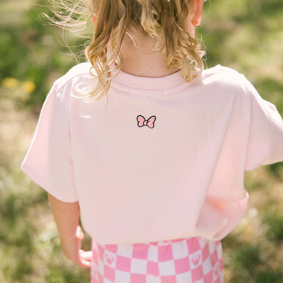 Close up back view of child wearing a pink Minnie Mouse t shirt for kids on a blurred background.