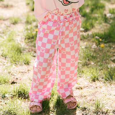 Child wearing pink checkered kid's Disney pants standing in a grassy area