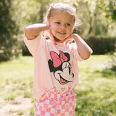 Young girl standing outside wearing a cute Minnie Mouse shirt for kids in pink.